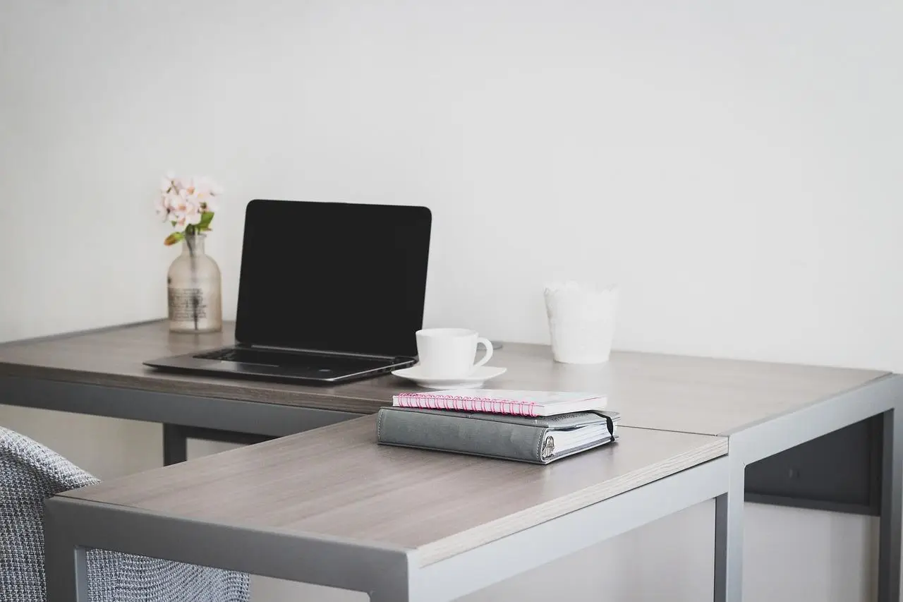 Een L-vormige tafel met een laptop erop.